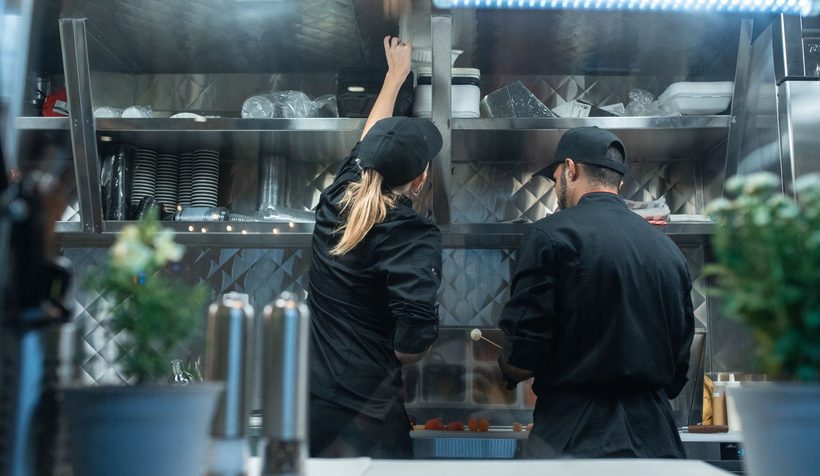 Two cooks working at a refrigerated prep station in a commercial kitchen